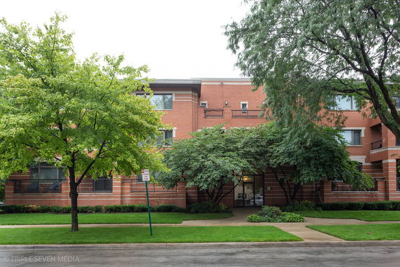 Front view of a multi-story brick building with trees and a pathway.
