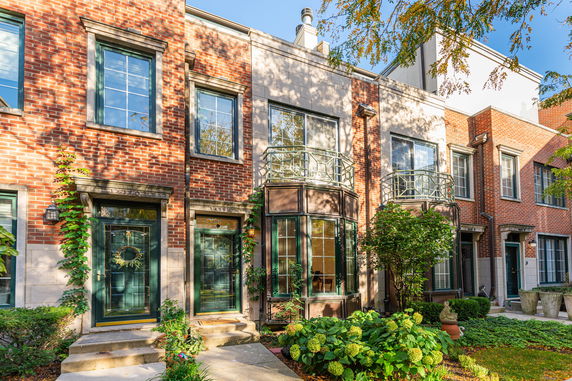 Front view of a two-story brick townhouse with large windows and green doors.