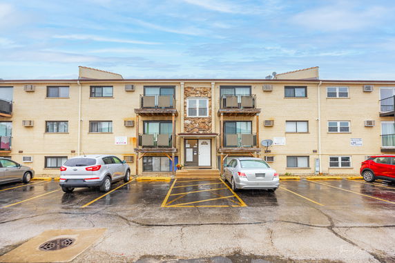 Front view of a three-story apartment building with parked cars in front.
