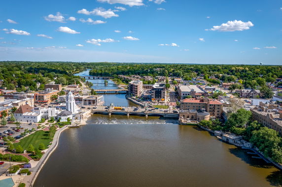 Panoramic view of a cityscape with a river, buildings, and green areas.