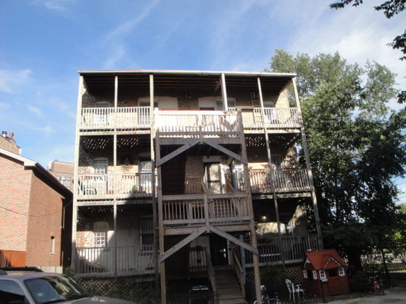Rear view of a multi-story residential building with balconies and exposed wooden staircases.