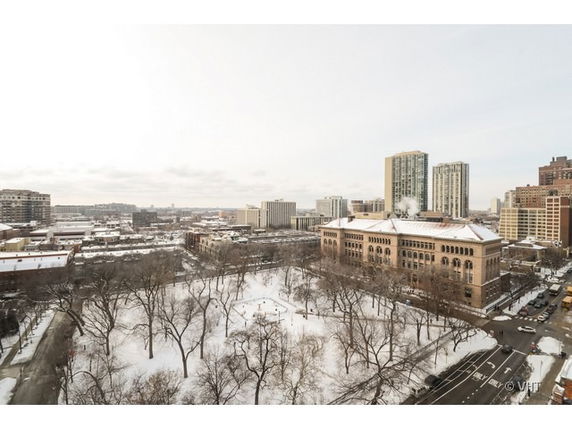 Aerial view of a cityscape with a large historic building and surrounding skyscrapers, visible over a snow-covered park.