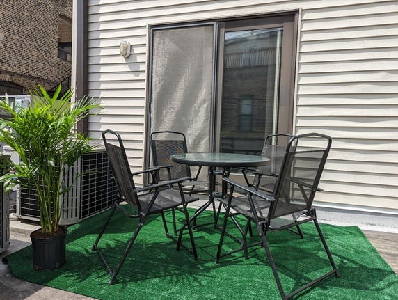 Rooftop area with a small table and chairs, artificial grass, and a potted plant.