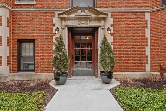 Front view of a brick building entrance with decorative columns and two potted plants.