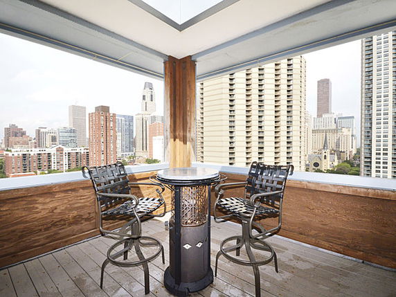 Rooftop area with two chairs and a table, with a view of surrounding buildings.
