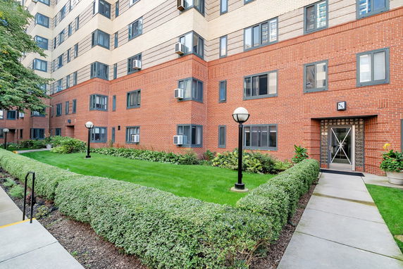 Front view of a multi-story brick apartment building with a well-maintained lawn and hedges.