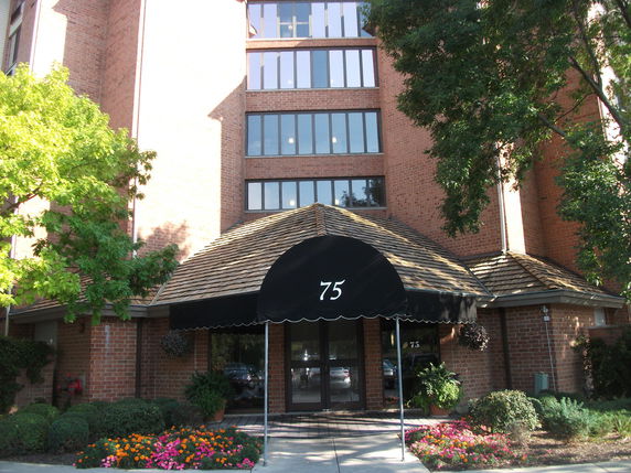 Front view of a brick multi-story building with a covered entrance marked '75'.
