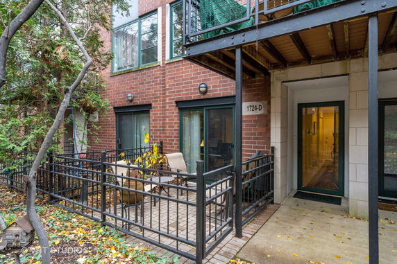 Front view of a brick apartment building with a small fenced patio area.