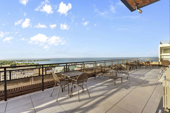 Rooftop with metal chairs and tables, ocean view in the background.