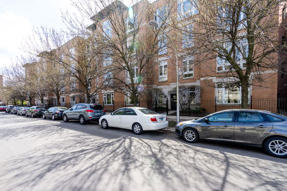 Front view of a multi-story building with parked cars and bare trees lining the street.