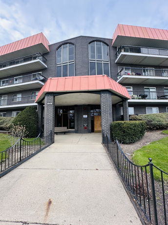 Front view of a multi-story brick building with balconies and red roofing.