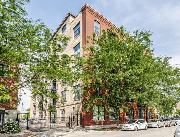 Front view of a multi-story brick building with large windows and a gated area in front.