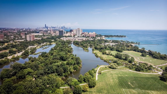Aerial panoramic view of a cityscape with expansive greenery and water bodies.
