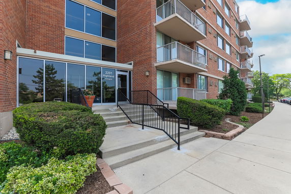 Front view of a multi-story brick apartment building with balconies and a glass entrance.