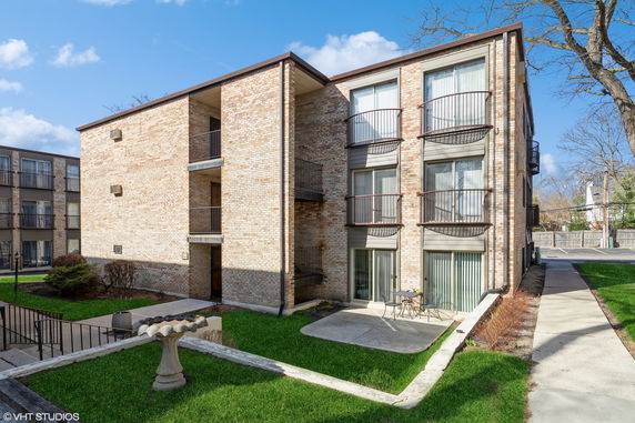 Front view of a multi-story brick apartment building with balconies and a small patio area.