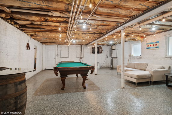 Room with a pool table and seating area in a basement setting.