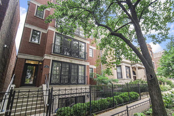 Front view of a multi-story brick house with black framed windows and a fenced entrance.