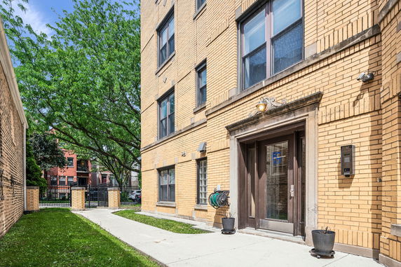 Front view of a multi-story brick building with a glass door entrance and intercom system.