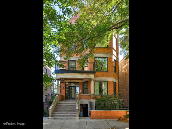 Front view of a three-story brick house with large windows and a staircase leading to the entrance.