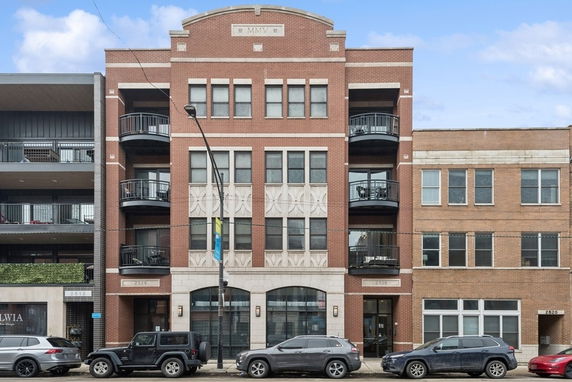 Front view of a multi-story brick building with balconies and arched entrance.