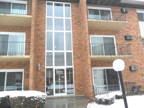 Front view of a multi-story brick building with balconies and large glass entrance.