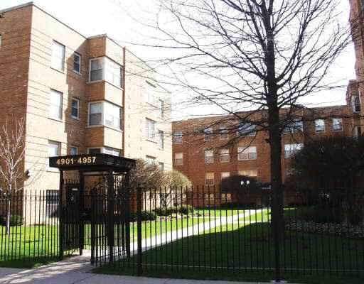 Front view of a multi-story brick apartment building with a gated entrance.