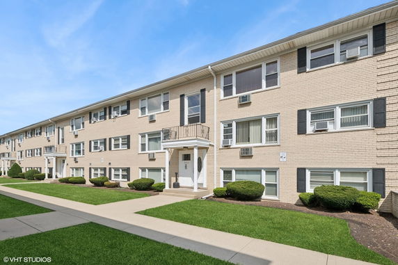 Front view of a multi-story apartment building with beige brick facade and several windows.