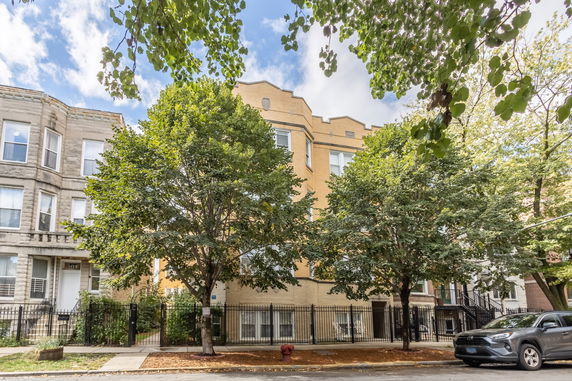 Front view of a multi-story brick building with trees and a fence.