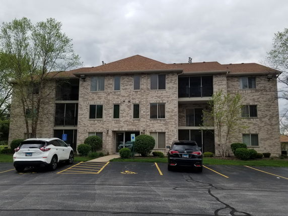 Front view of a three-story apartment building with a parking area in front.