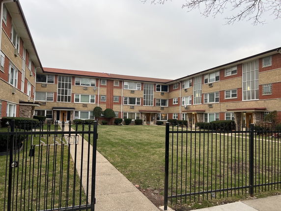 Front view of a three-story apartment building with a central entrance and a gated courtyard.
