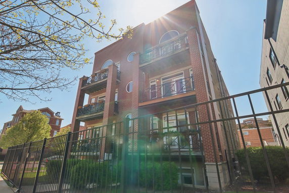 Front view of a brick apartment building with multiple balconies and a metal fence.