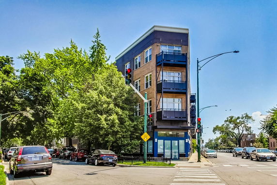 Front view of a multi-story building on a street corner with balconies and large windows.