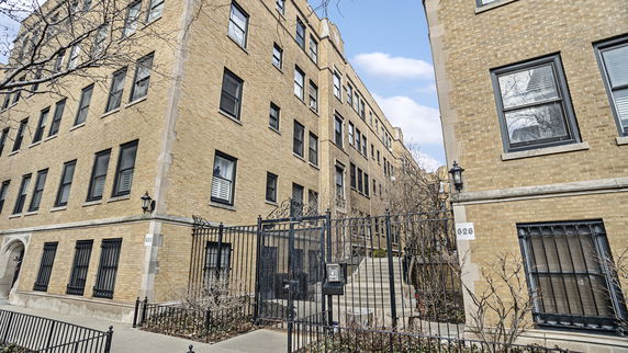 Front view of a multi-story brick apartment building with a gated entrance.