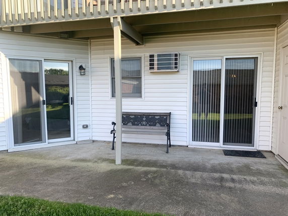 Front view of a building with a patio area, sliding glass doors, and an air conditioning unit.