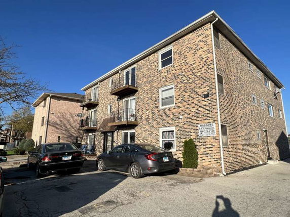 Front view of a three-story brick apartment building with balconies.