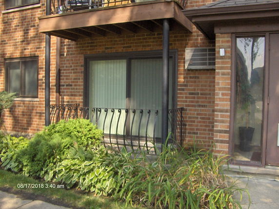 Front view of a brick building with a small balcony and air conditioning unit.