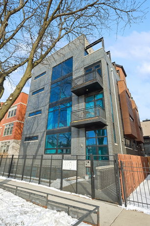 Front view of a modern multi-story building with large windows and a balcony.