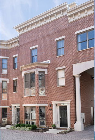 Front view of a multi-story brick townhouse with a bay window and columned entryway.