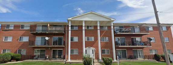 Front view of a three-story brick apartment building with balconies.