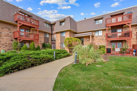 Front view of a multi-story brick apartment building with balconies and a sloped roof.