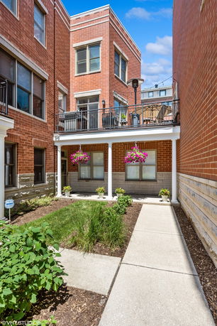 Front view of a multi-story brick building with balconies and decorative plants.