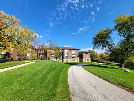 Front view of a multi-story brick building with a paved walkway and surrounding greenery.
