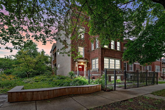 Front view of a brick multi-story house with a fenced front yard.