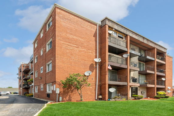 Front view of a multi-story brick apartment building with balconies and satellite dishes.