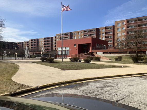 Front view of a multi-story apartment building with a red facade and flagpole.