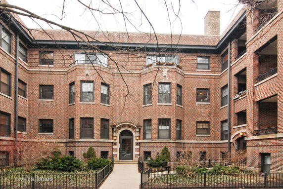 Front view of a multi-story brick apartment building with bay windows and an arched entrance.