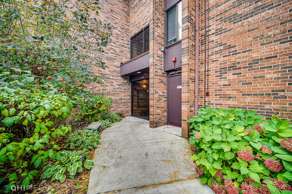 Front view of a brick-walled building entrance with surrounding greenery.