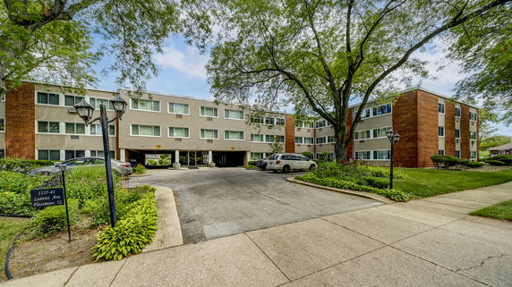 Front view of a multi-story residential building with a driveway and parking area.