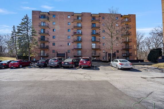 Front view of a multi-story apartment building with balconies and parked cars in front.