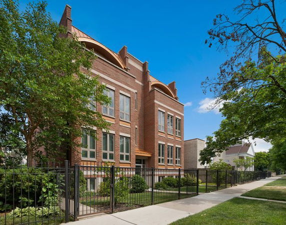Front view of a multi-story brick building with large windows and a fenced perimeter.
